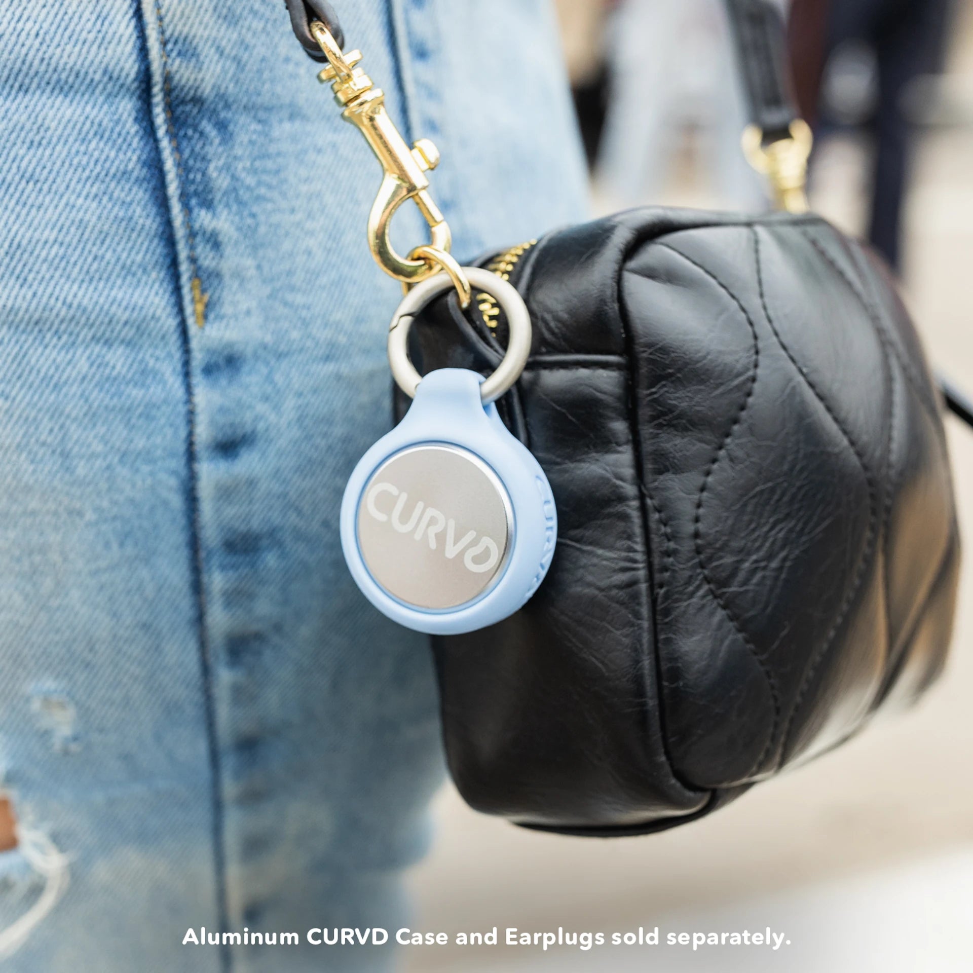 A light blue CURVD aluminum earplug case attached to a black quilted handbag, providing an elegant and accessible storage solution for earplugs.