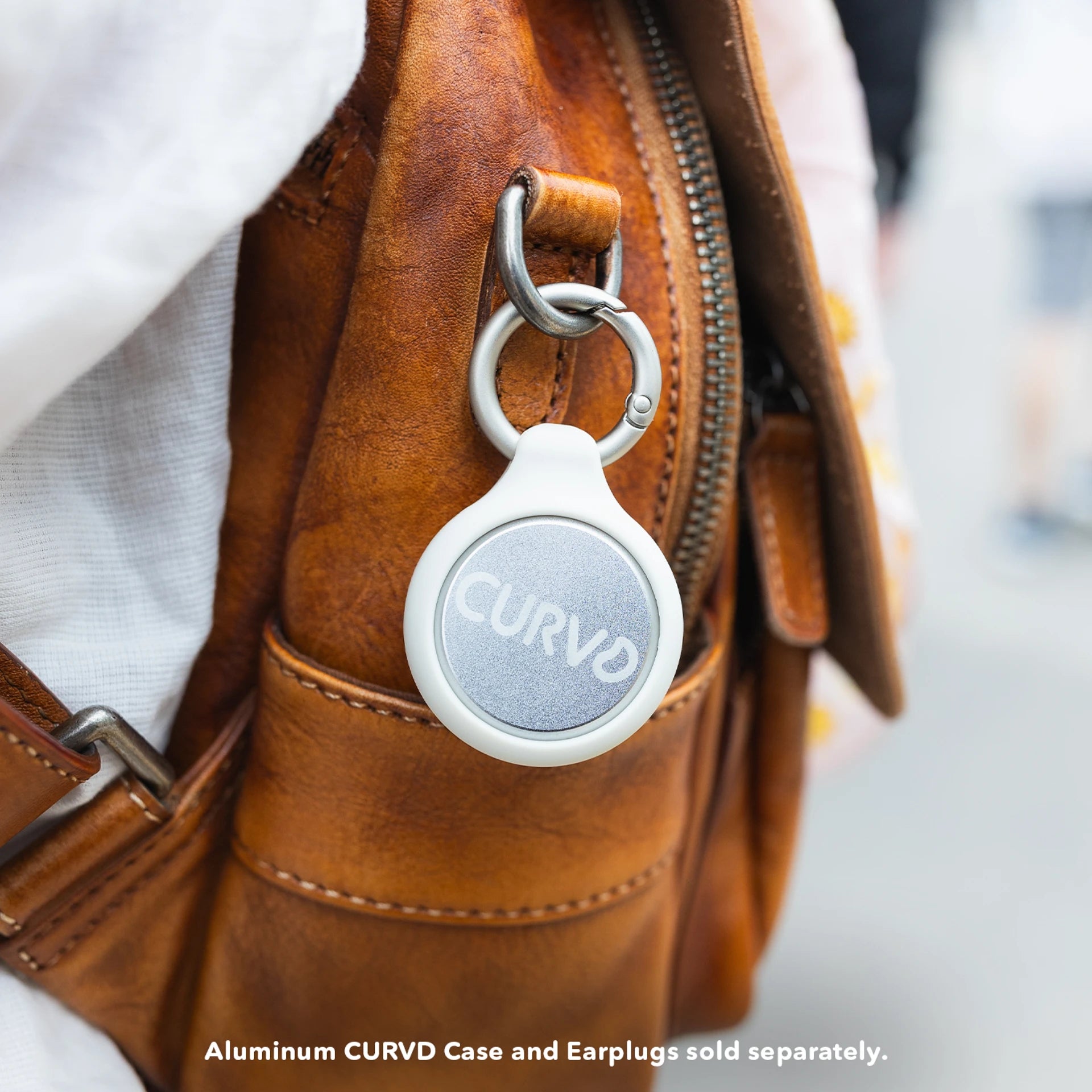 A Honey CURVD aluminum earplug case clipped to a brown leather backpack, combining practicality with a sleek, minimalist design.