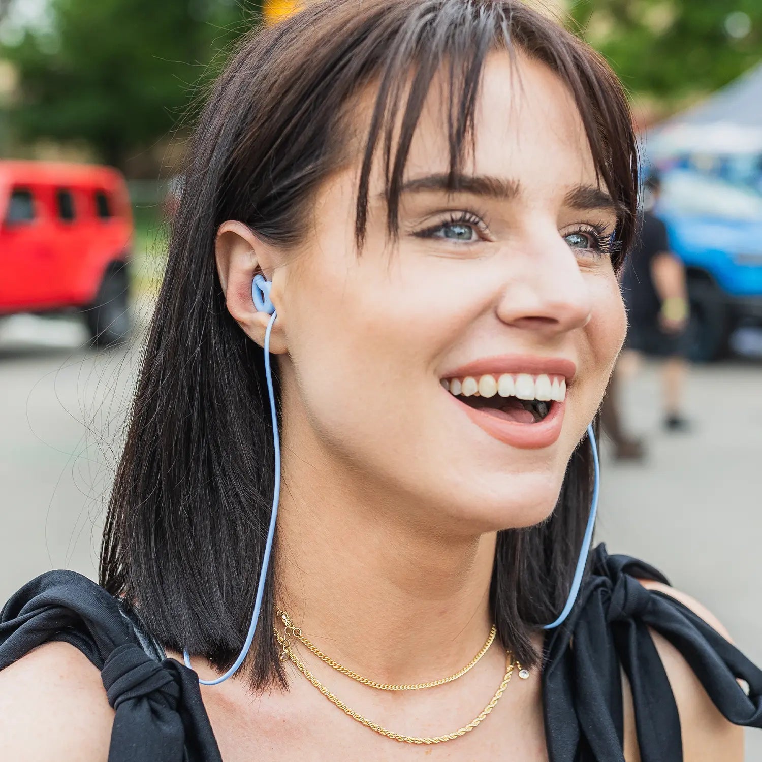 Woman wearing CURVD earplugs with a blue lanyard at an outdoor event, smiling and looking engaged.