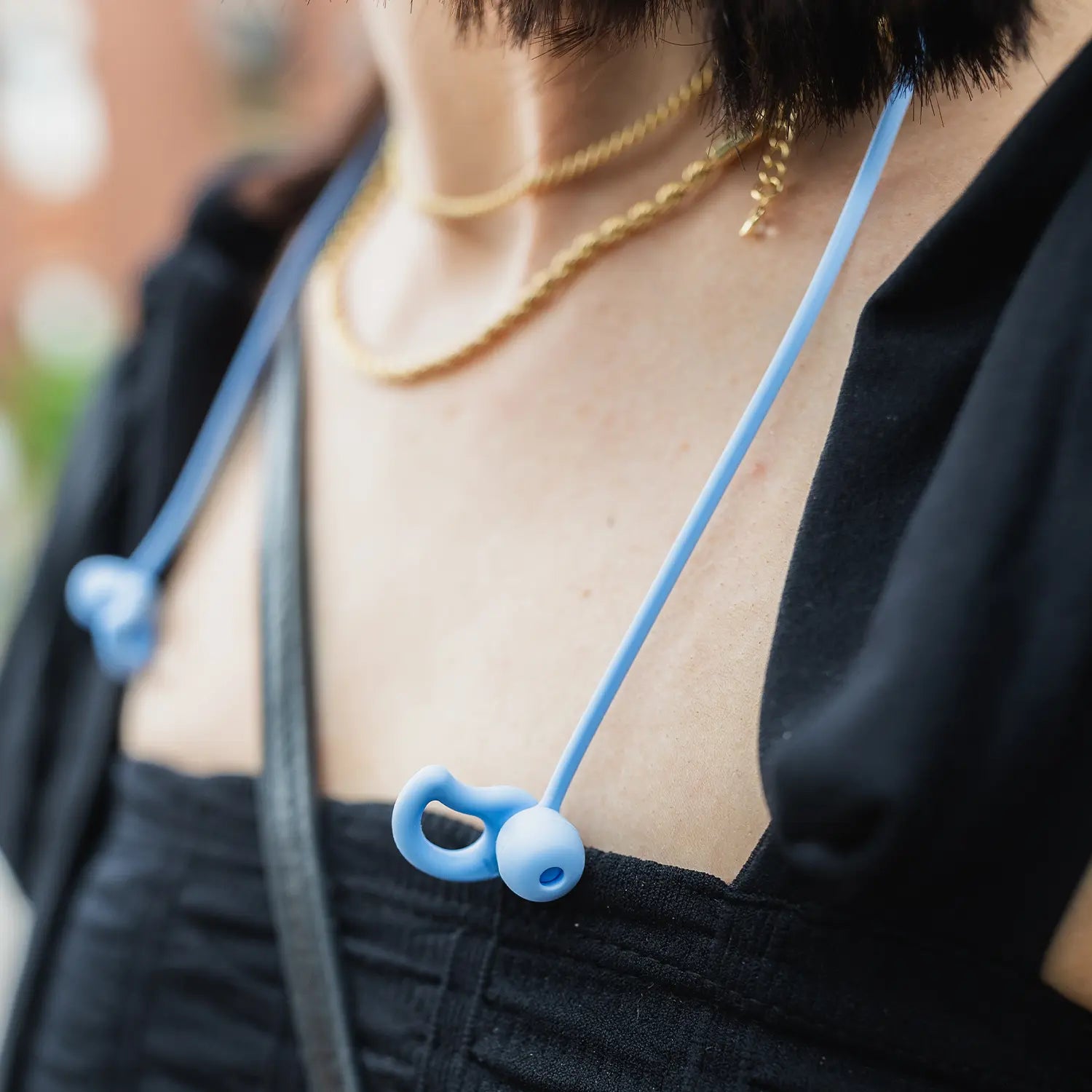 Close-up of CURVD earplugs with a blue lanyard resting around a woman’s neck, highlighting the stylish design and convenient accessibility.